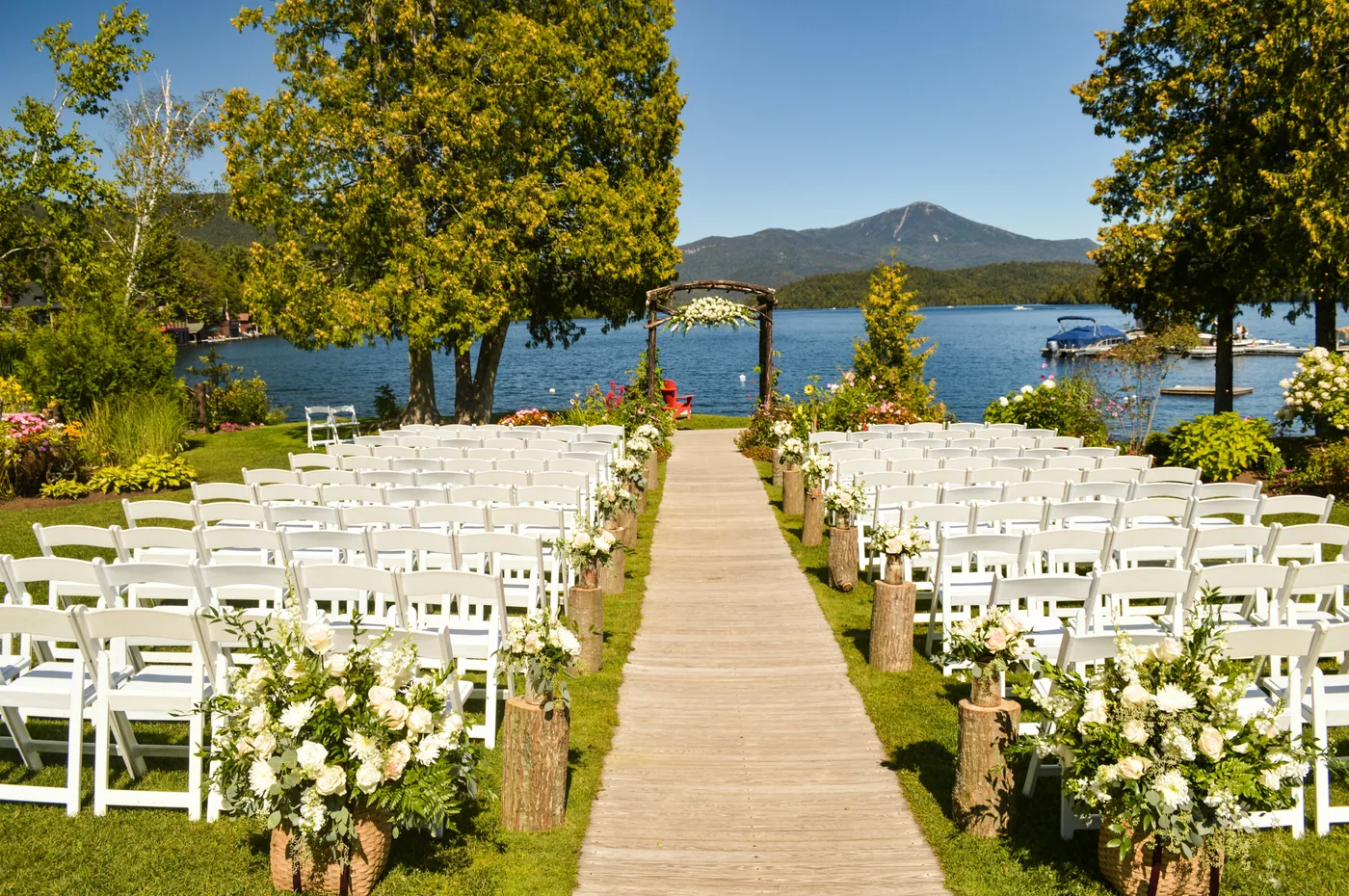 Trauzeremonie im Freien mit Seeblick, Holzstümpfen mit Blumen und weißer Bestuhlung